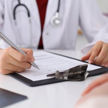 Close up of a female doctor filling up  an application form while consulting patient