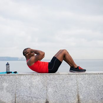 Man doing sit ups. Core outdoor workout. Black athlete exercising.