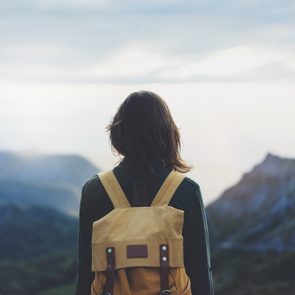 Hipster young girl with bright backpack enjoying sunset on peak of foggy mountain. Tourist traveler on background valley landscape view mockup. Hiker looking sunlight flare in trip Picos de Europa