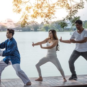 Group of young people practicing traditional Tai Chi Chuan, Tai Ji  and Qi Gong for fighting match together in the park on the lake background, traditional chinese martial arts concept.