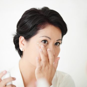 Beautiful female applying facial treatment or cream around her eyes.