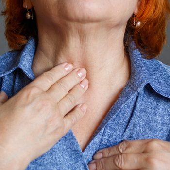 An elderly woman feels her thyroid gland.