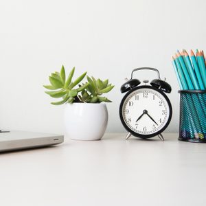 desk with laptop clock plant and pencils