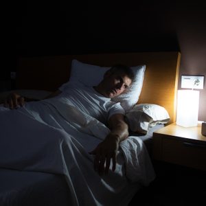 A man with insomnia looks at the clock at dawn from the bed with concern